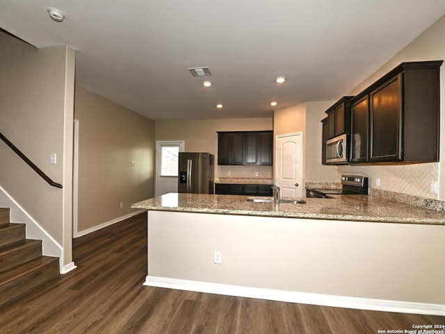 kitchen with dark hardwood / wood-style floors, light stone counters, kitchen peninsula, and appliances with stainless steel finishes