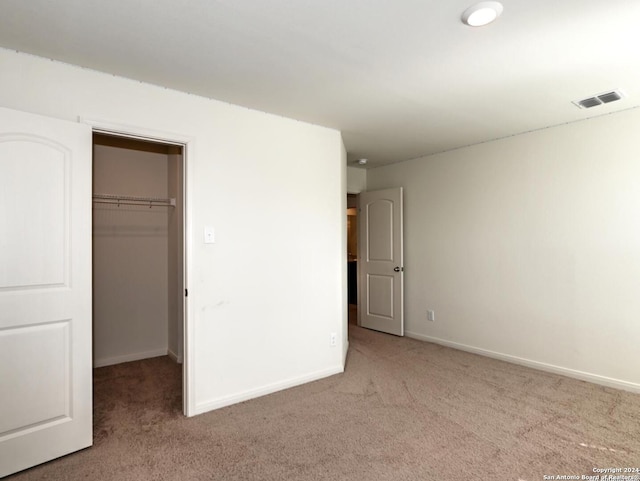 unfurnished bedroom featuring a spacious closet, a closet, and light colored carpet