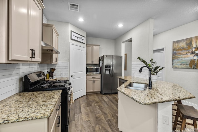 kitchen featuring sink, stainless steel appliances, light stone counters, range hood, and a breakfast bar area