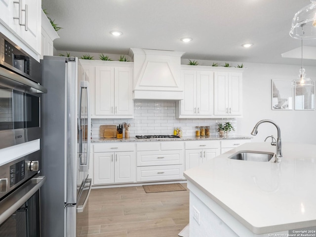 kitchen featuring sink, stainless steel appliances, light hardwood / wood-style floors, white cabinets, and custom exhaust hood