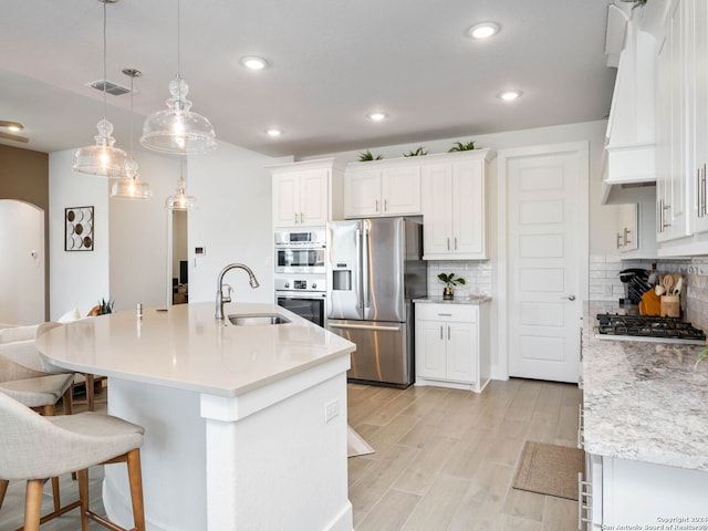 kitchen featuring sink, an island with sink, appliances with stainless steel finishes, decorative light fixtures, and white cabinetry