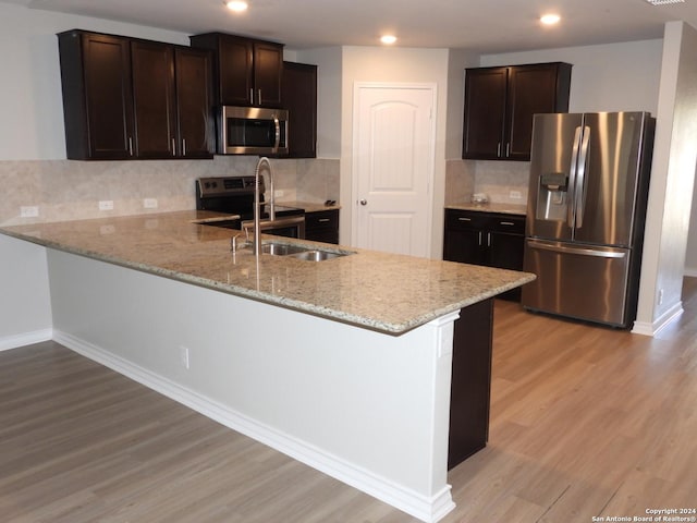 kitchen featuring backsplash, kitchen peninsula, stainless steel appliances, and light wood-type flooring