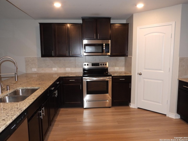 kitchen featuring backsplash, sink, light stone countertops, light wood-type flooring, and stainless steel appliances