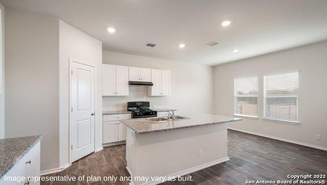 kitchen featuring black gas range, sink, dark wood-type flooring, a kitchen island with sink, and white cabinets