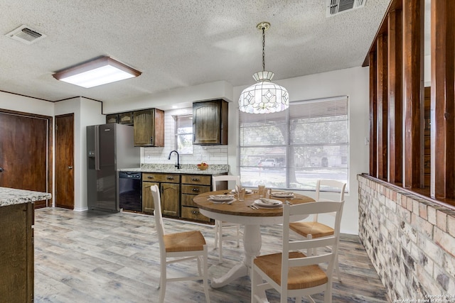 kitchen featuring a textured ceiling, light wood-type flooring, black dishwasher, and hanging light fixtures