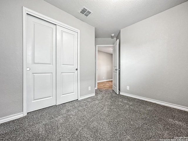 unfurnished bedroom with a textured ceiling, dark carpet, and a closet