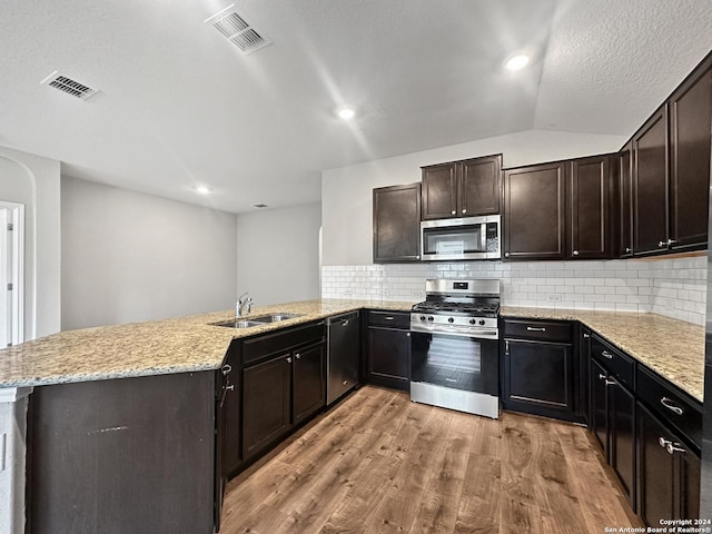 kitchen featuring kitchen peninsula, appliances with stainless steel finishes, light wood-type flooring, tasteful backsplash, and sink