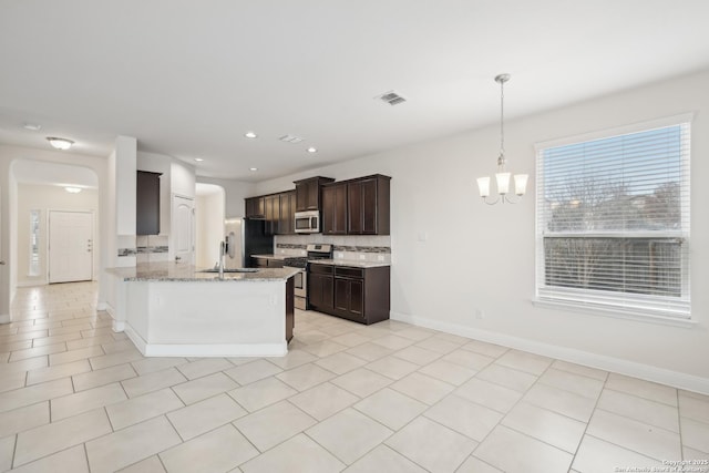 kitchen featuring sink, tasteful backsplash, appliances with stainless steel finishes, a notable chandelier, and light stone countertops