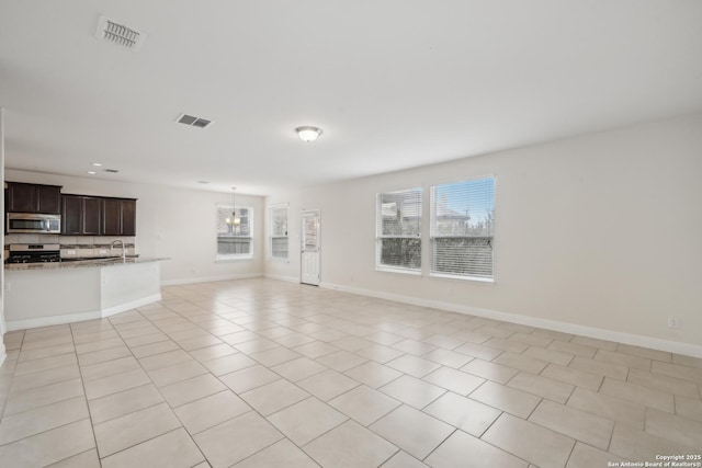 unfurnished living room with an inviting chandelier, sink, light tile patterned floors, and a wealth of natural light