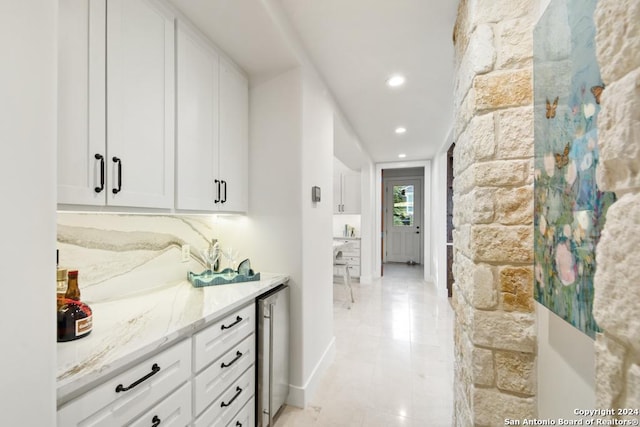 bar featuring wine cooler, white cabinetry, and light stone counters