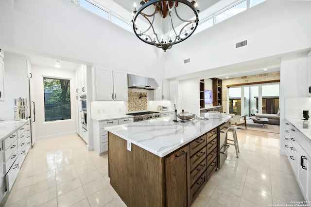 kitchen featuring decorative backsplash, wall chimney range hood, an inviting chandelier, white cabinets, and a kitchen island