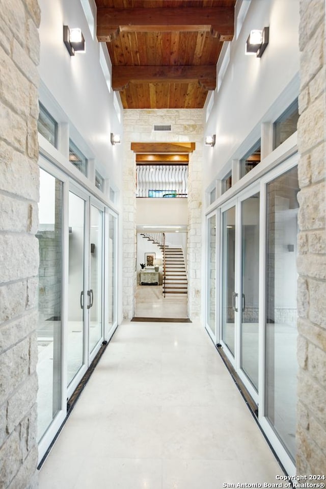 hall featuring beamed ceiling, wooden ceiling, a towering ceiling, and french doors