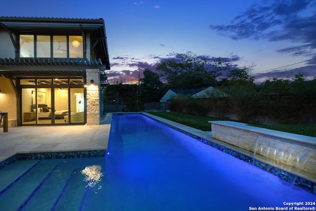 pool at dusk featuring pool water feature and a patio