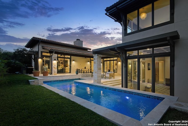 back house at dusk featuring a patio area and a yard