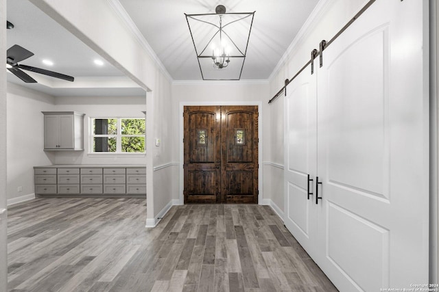 entryway with ceiling fan with notable chandelier, a barn door, crown molding, and light hardwood / wood-style flooring