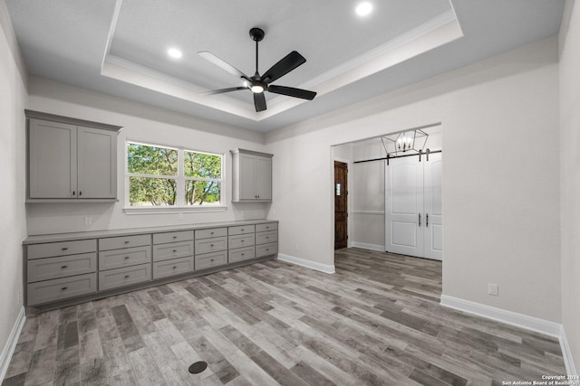 unfurnished bedroom with a raised ceiling, crown molding, light hardwood / wood-style flooring, and ceiling fan with notable chandelier