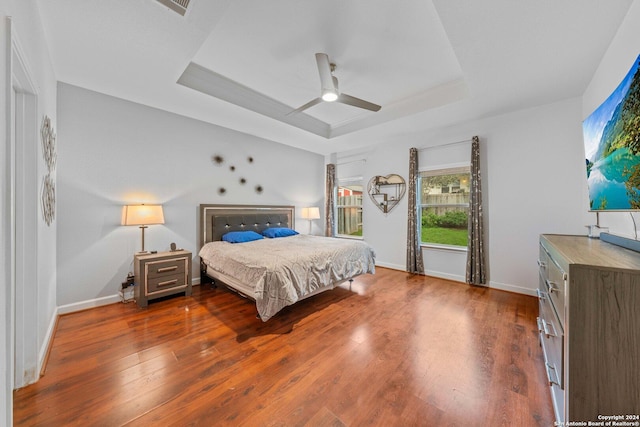 bedroom with ceiling fan, dark hardwood / wood-style flooring, and a tray ceiling