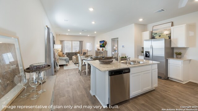 kitchen with white cabinetry, sink, stainless steel appliances, hardwood / wood-style floors, and a kitchen island with sink