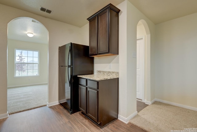 kitchen featuring hardwood / wood-style flooring, dark brown cabinets, black fridge, and light stone countertops