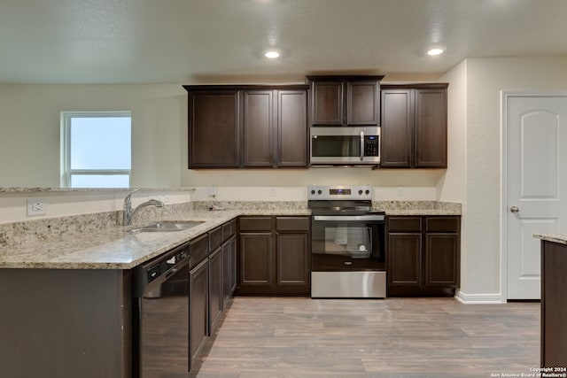 kitchen with light stone countertops, appliances with stainless steel finishes, light wood-type flooring, dark brown cabinets, and sink