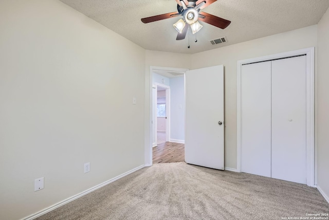 unfurnished bedroom featuring a textured ceiling, a closet, ceiling fan, and light colored carpet