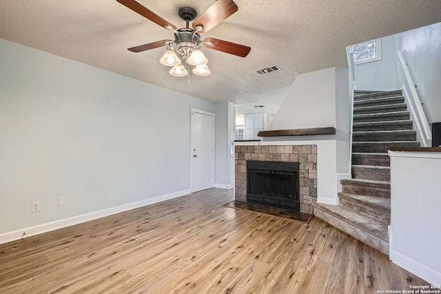 unfurnished living room with ceiling fan, light hardwood / wood-style floors, a textured ceiling, and a fireplace