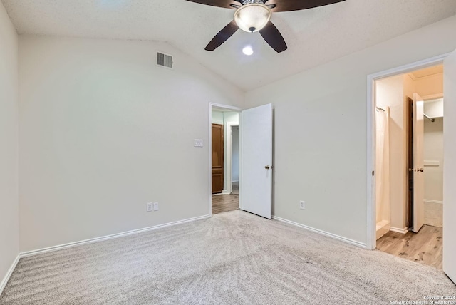 unfurnished bedroom featuring ensuite bathroom, ceiling fan, light colored carpet, and vaulted ceiling