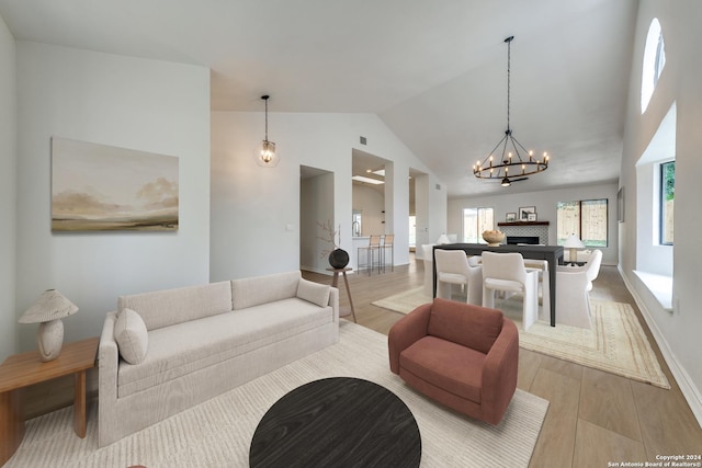 living room featuring high vaulted ceiling, light hardwood / wood-style floors, an inviting chandelier, and a healthy amount of sunlight