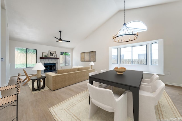 dining room featuring ceiling fan with notable chandelier, light wood-type flooring, high vaulted ceiling, and a tile fireplace