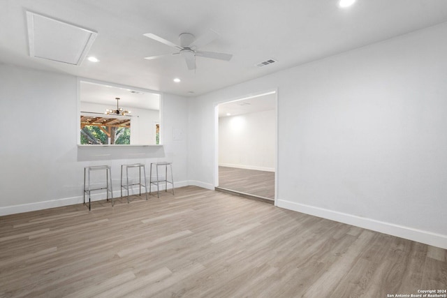 empty room featuring ceiling fan with notable chandelier and light hardwood / wood-style flooring