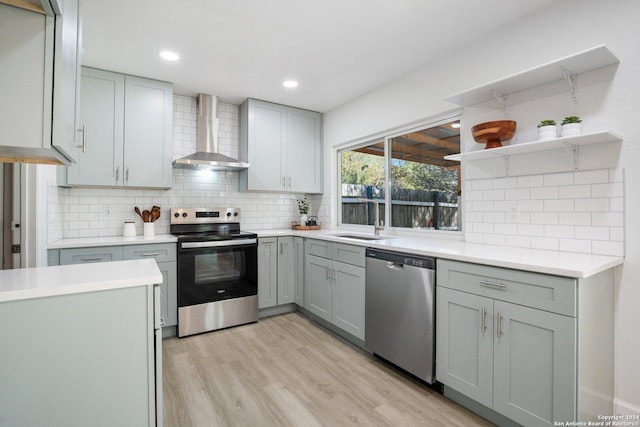 kitchen with backsplash, wall chimney exhaust hood, stainless steel appliances, sink, and light hardwood / wood-style flooring