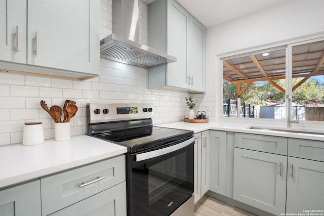 kitchen with sink, wall chimney exhaust hood, backsplash, stainless steel electric range, and light wood-type flooring