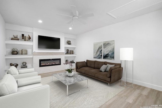 living room featuring ceiling fan, light hardwood / wood-style floors, a fireplace, and built in shelves