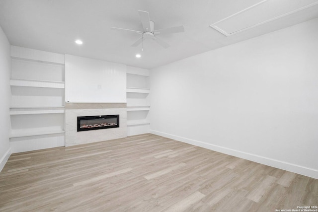 unfurnished living room featuring ceiling fan, built in shelves, a high end fireplace, and light hardwood / wood-style flooring