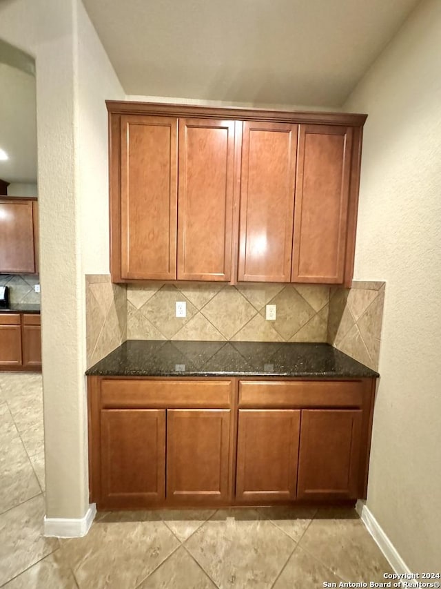 kitchen with light tile patterned floors, backsplash, and dark stone countertops