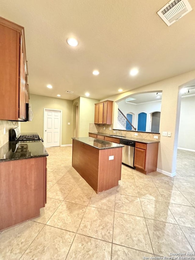 kitchen with appliances with stainless steel finishes, tasteful backsplash, dark stone counters, sink, and a kitchen island