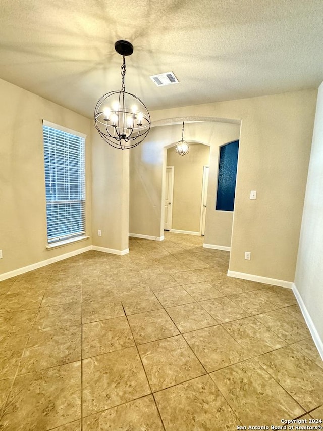 unfurnished dining area featuring a textured ceiling and an inviting chandelier