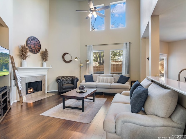 living room featuring a towering ceiling, dark hardwood / wood-style floors, ceiling fan, and a tiled fireplace