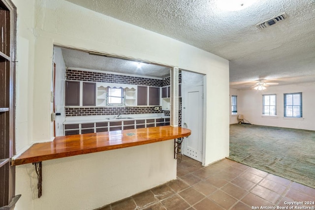 kitchen featuring ceiling fan, wooden counters, tile patterned floors, backsplash, and a textured ceiling