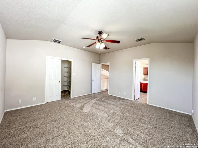 unfurnished bedroom with a walk in closet, a textured ceiling, light colored carpet, ceiling fan, and connected bathroom