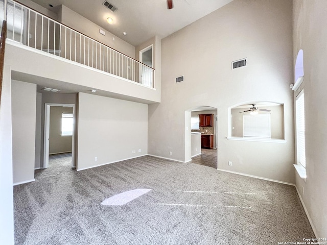 unfurnished living room featuring a towering ceiling, carpet floors, and ceiling fan