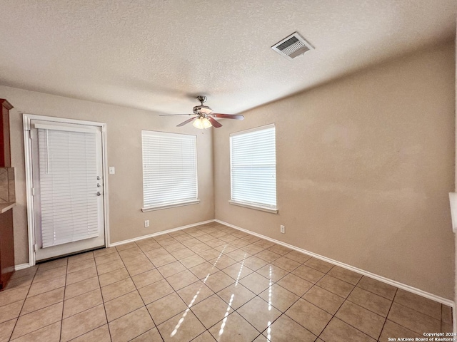 empty room with ceiling fan, light tile patterned floors, and a textured ceiling