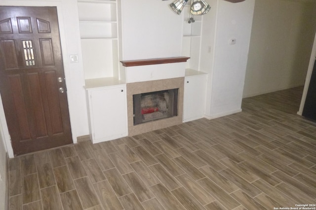 unfurnished living room with ceiling fan, dark wood-type flooring, and a tiled fireplace