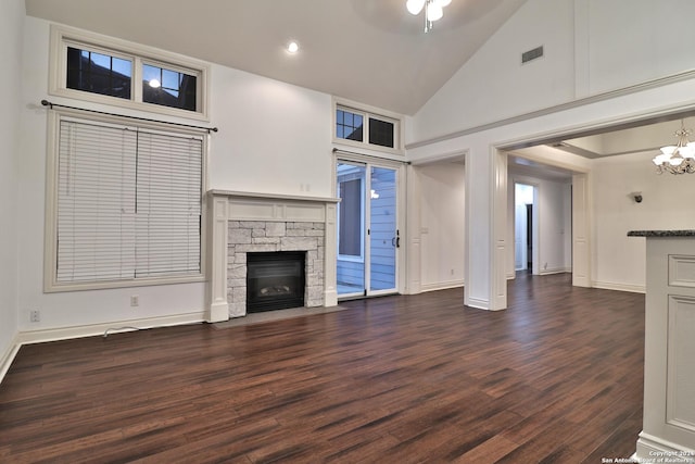 unfurnished living room with ceiling fan with notable chandelier, a stone fireplace, dark wood-type flooring, and high vaulted ceiling