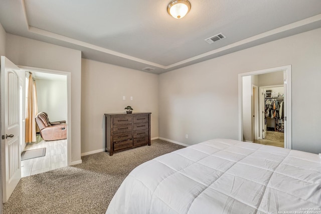 carpeted bedroom with a walk in closet, a raised ceiling, and a closet