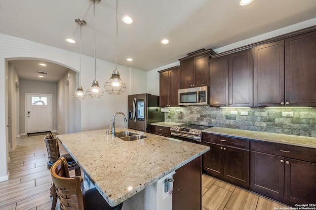 kitchen featuring appliances with stainless steel finishes, light stone counters, sink, hanging light fixtures, and an island with sink