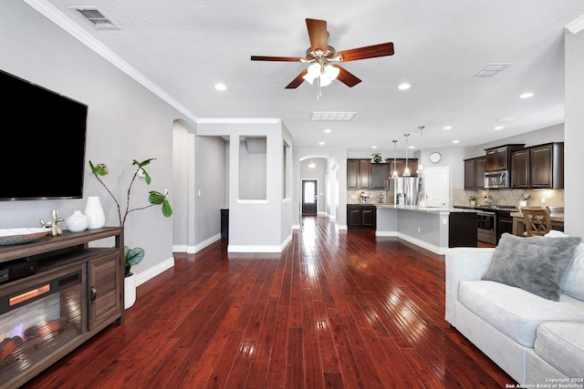 living room featuring dark hardwood / wood-style flooring, ornamental molding, a textured ceiling, ceiling fan, and sink