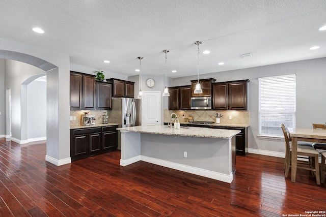 kitchen with sink, dark hardwood / wood-style flooring, an island with sink, decorative light fixtures, and appliances with stainless steel finishes