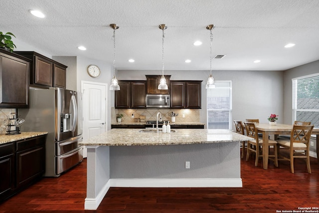 kitchen featuring stainless steel appliances, hanging light fixtures, dark wood-type flooring, and a kitchen island with sink