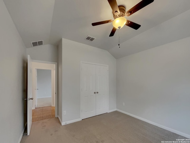 unfurnished bedroom featuring ceiling fan, a closet, light carpet, and vaulted ceiling